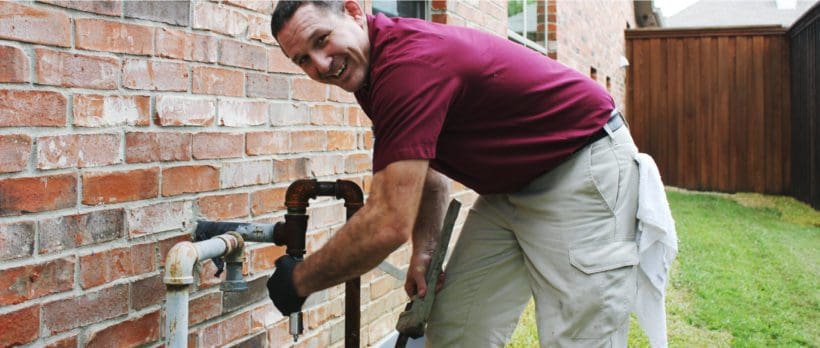 image of legacy technician working on gas pipe at gas meter near house brick wall